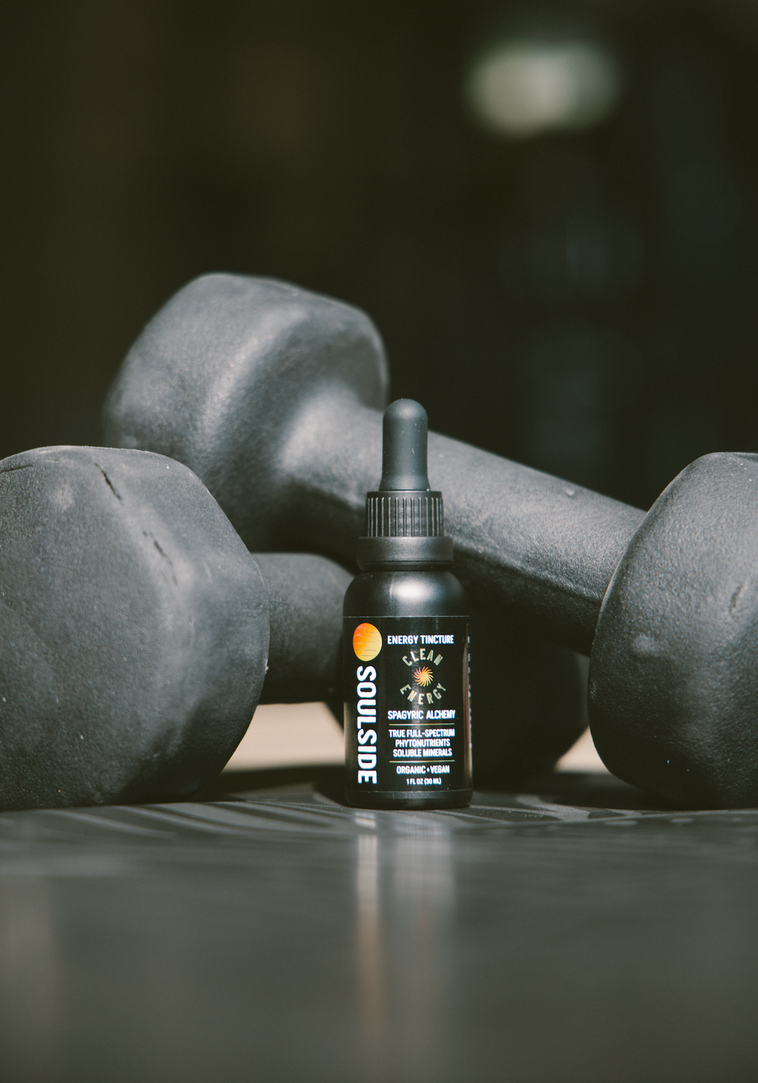 Image of Soulside Clean Energy tincture, an herbal tincture for energy, focus, athletic performance, endurance, in front of gym weights, implying its use as a pre-workout solution.