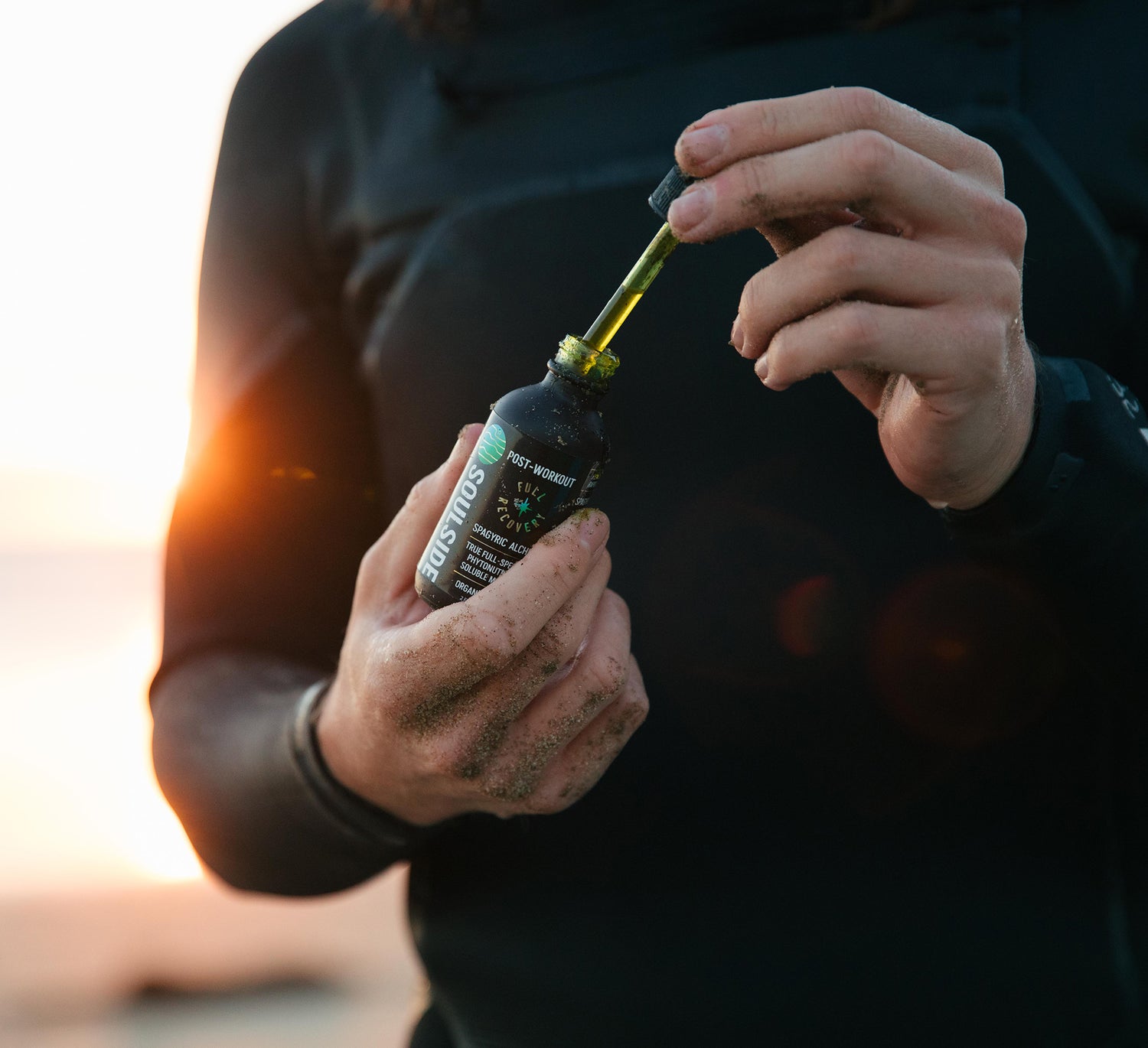 Image of a surfer holding Soulside 2oz recovery tincture, an organic herbal extraction for muscle build, fatigue, recovery, soreness, brain health and immunity.